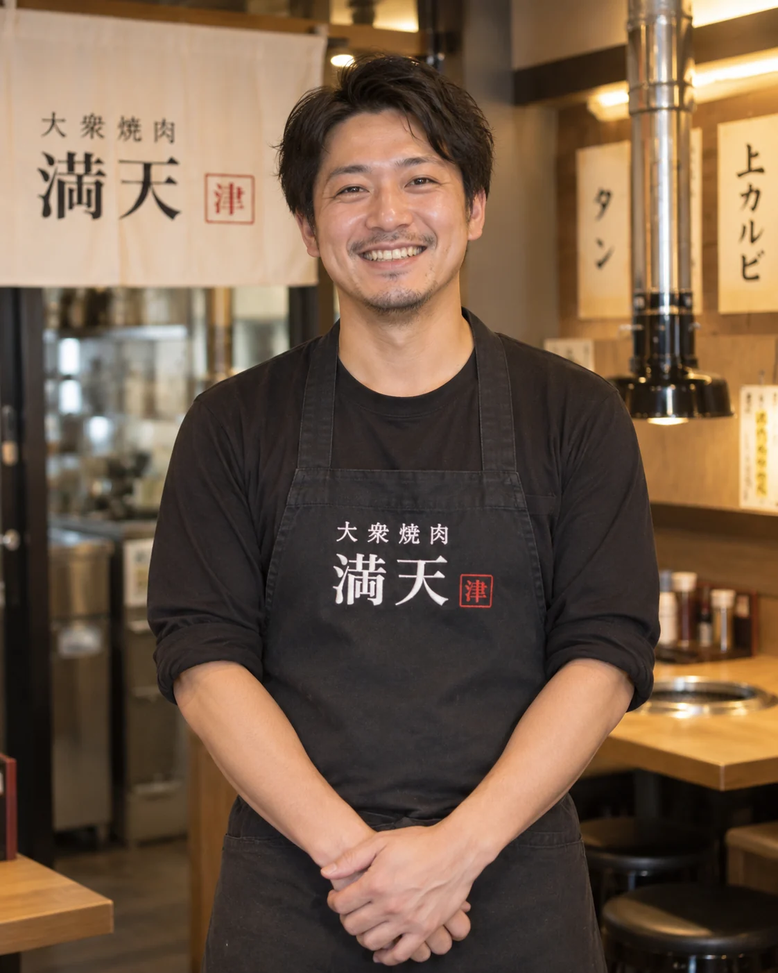 満天の前掛けを着け、店内で笑顔を見せる店主